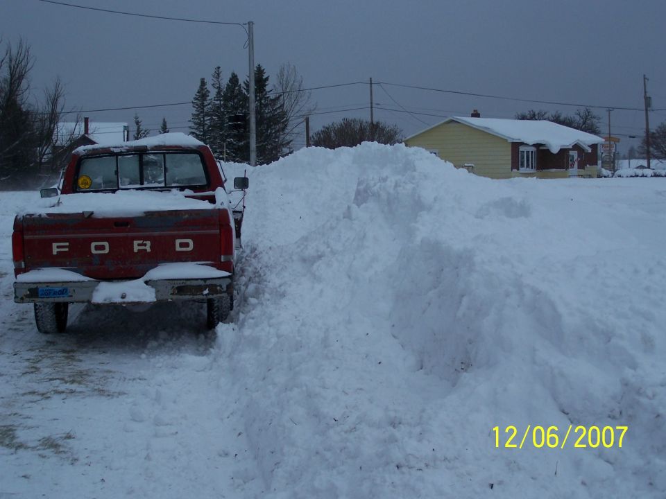 Rear view of a red Ford pickup truck partially covered in snow, parked next to a large snowdrift. Date stamp reads 12/06/2007