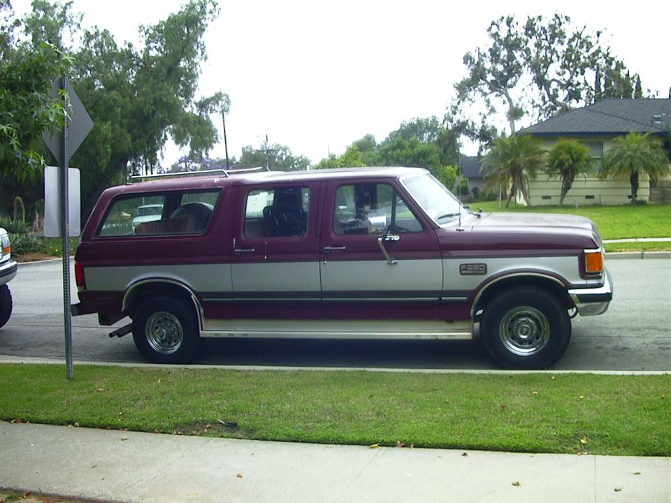 Burgundy and silver Ford SUV with four doors parked in profile on a residential street.
