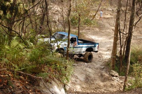 1982 Ford F-100 - A lifted pickup truck navigates a wooded trail, with a person visible in the distance.