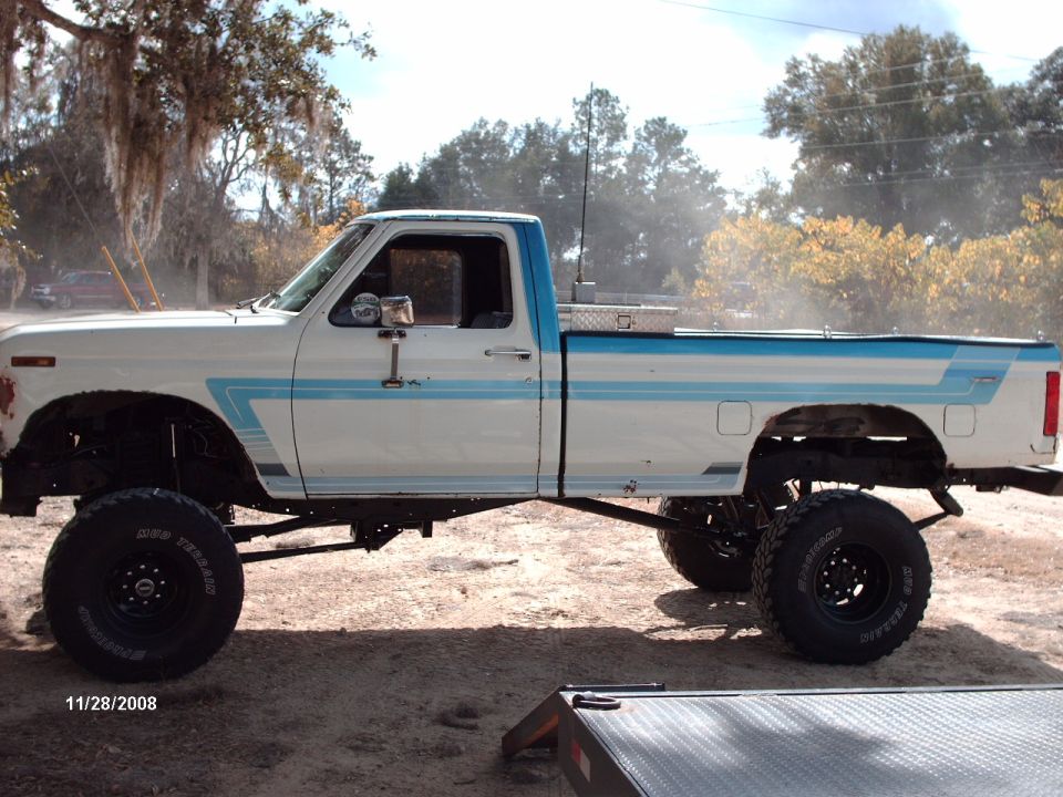 Lifted white pickup truck with blue trim, side view. Has big tires and a toolbox in the bed