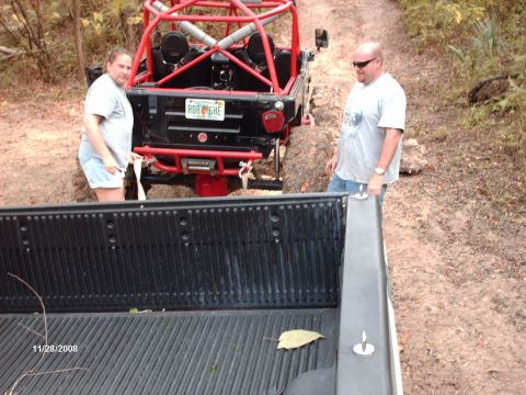 1982 Ford F-100 - Two people stand near a modified off-road vehicle stuck in mud on a dirt path.
