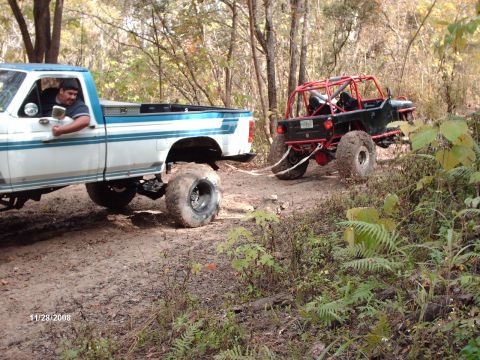 1982 Ford F-100 - A lifted Ford pickup truck tows a custom buggy through a wooded area on a dirt path.