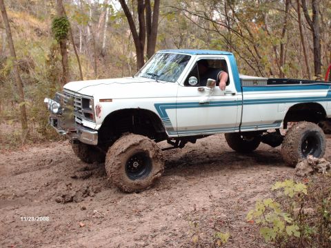 1982 Ford F-100 - Pickup truck with lifted suspension and large tires navigates a muddy off-road trail.