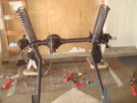 1992 Ford Bronco - A vehicle's front axle assembly, complete with suspension components, is shown disassembled in a garage setting.
