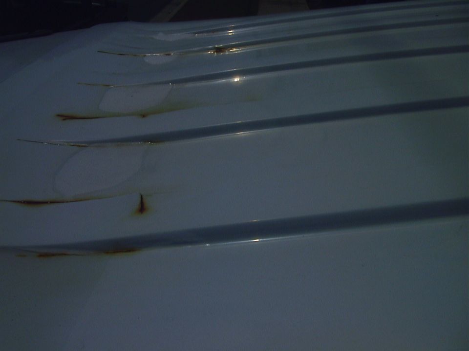 Close-up of white ribbed roof panel with rust streaks along the ridges