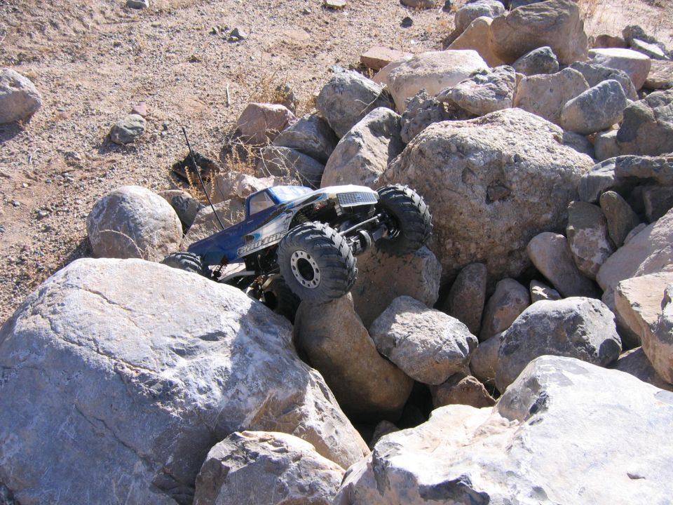 Blue and silver RC rock crawler truck with large tires climbing over rocks