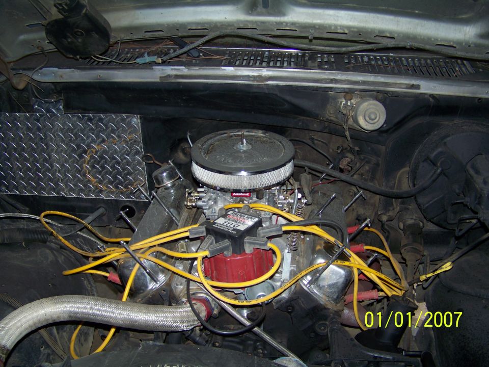 Engine bay with V8 engine, chrome air cleaner, and yellow spark plug wires. Diamond plate panel on left