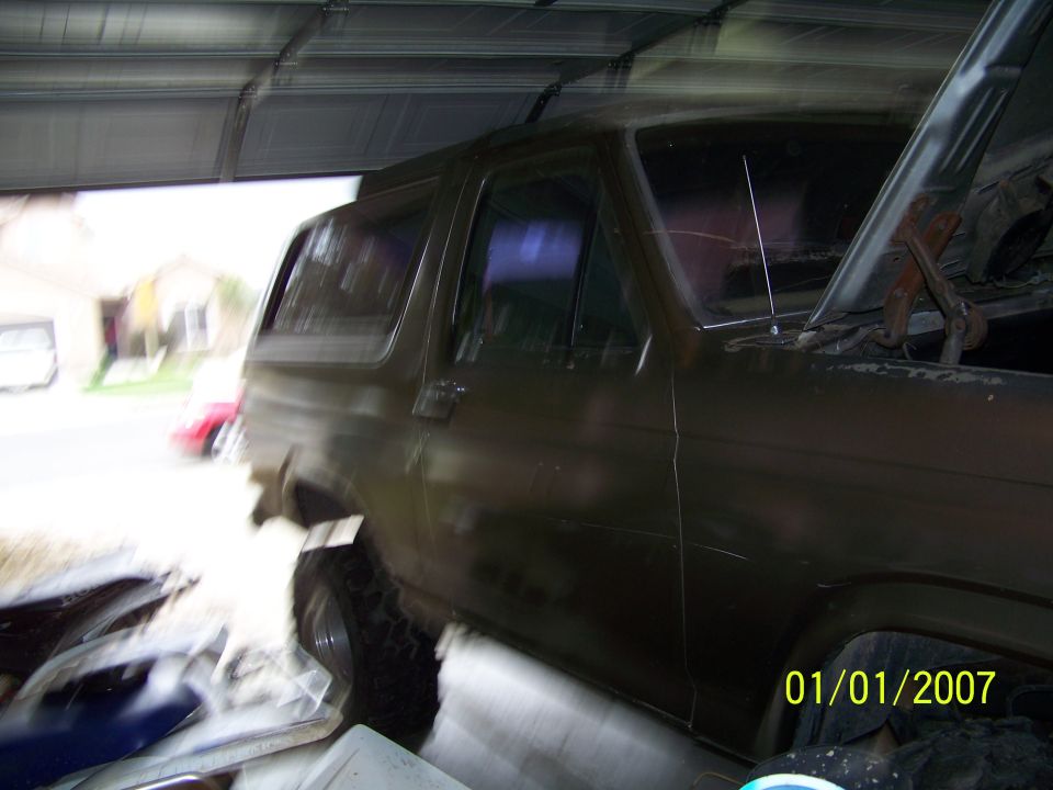 Side view of a dark-colored Ford Bronco, hood open, parked in a garage