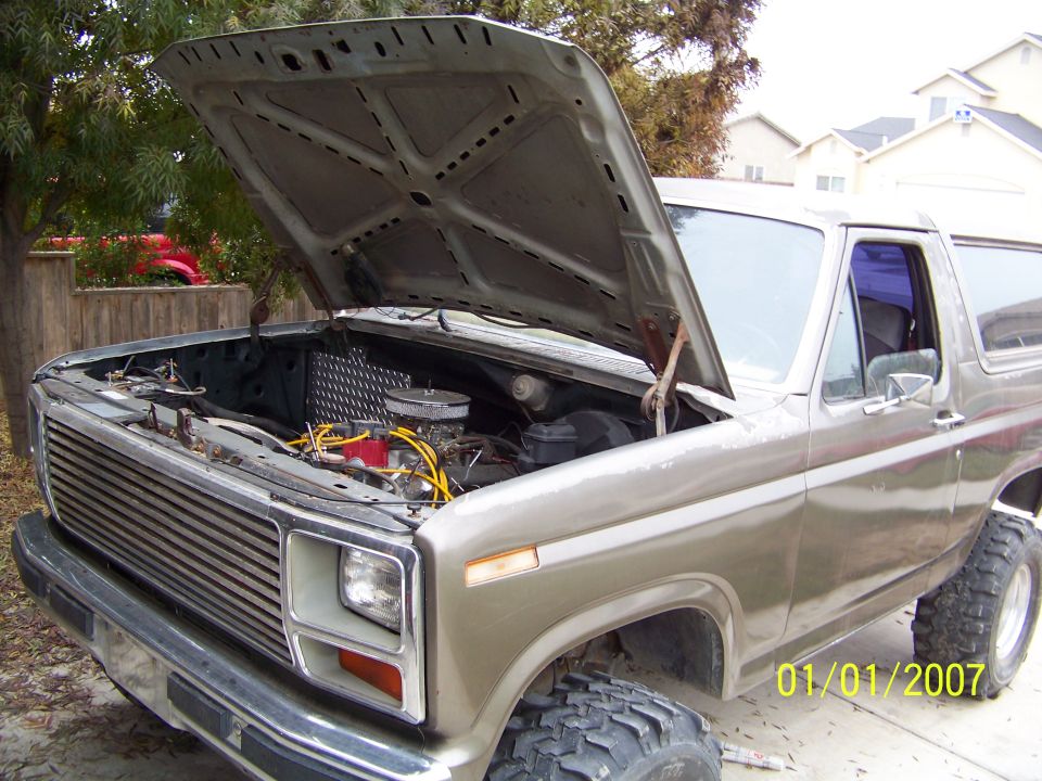 Tan Ford Bronco with hood open, showing engine and chrome grille