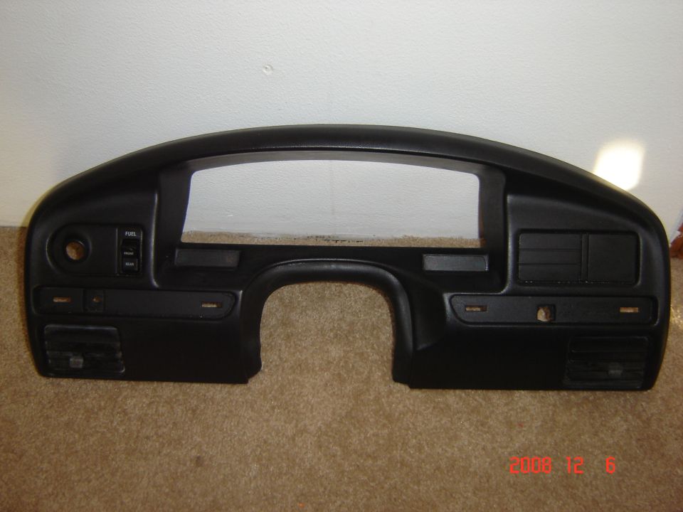 Black dashboard instrument bezel trim panel on carpet with gauge opening and vents