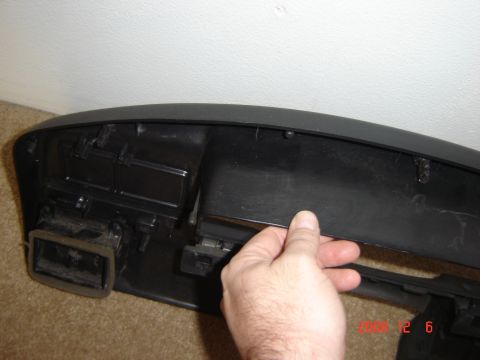 1993 Ford Bronco - A hand is shown holding a black plastic trim piece, likely from a vehicle's dashboard, revealing internal mounting points.