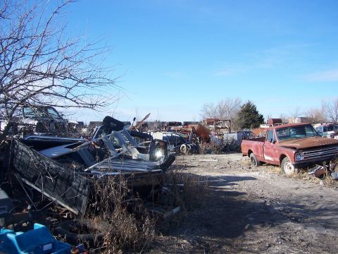 1979 Ford Bronco - A weathered red pickup truck sits in a junkyard, its grille indicating a 1967 model year.
