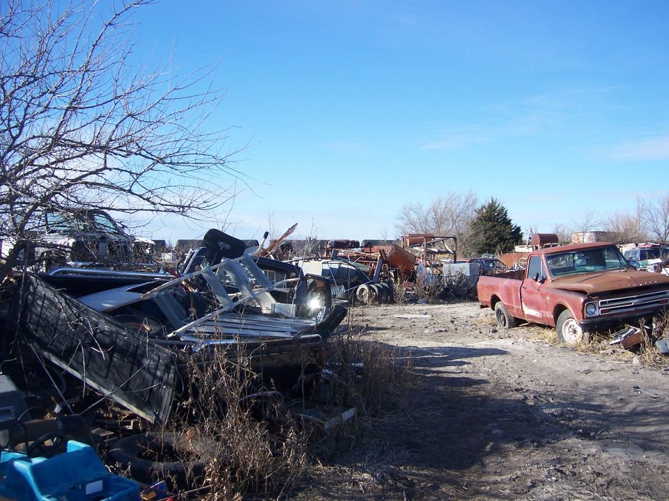 Rusty red pickup truck in a junkyard, 3q-front view. Grille suggests 1967