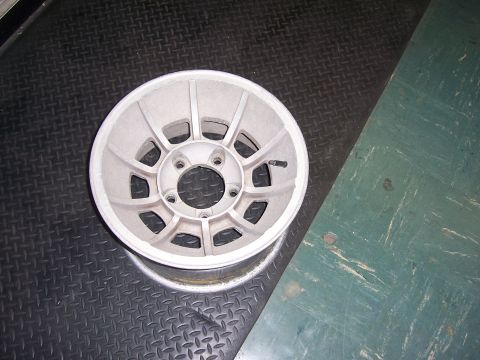 1979 Ford Bronco - A single aluminum wheel is shown on a textured surface, with a green painted area in the background.