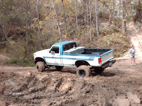 1982 Ford F-100 - A lifted Ford pickup truck navigates a muddy trail with trees in the background.