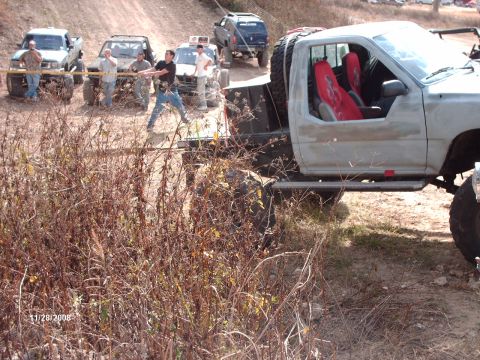 1982 Ford F-100 - Several off-road vehicles are engaged in a tug-of-war on a dirt track, with one truck bright red interior seats.