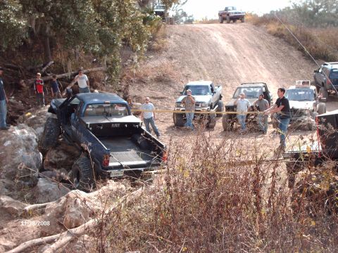 1982 Ford F-100 - Off-road trucks tackle a challenging rocky and dirt trail with spectators present.