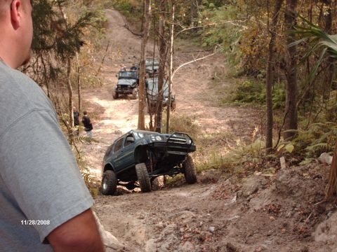 1982 Ford F-100 - Multiple off-road vehicles navigate a wooded dirt trail on a sunny day.