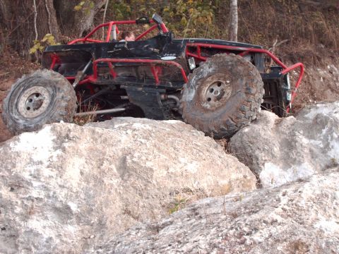 1982 Ford F-100 - This heavily modified Jeep is navigating a difficult rocky terrain, with one wheel high in the air.