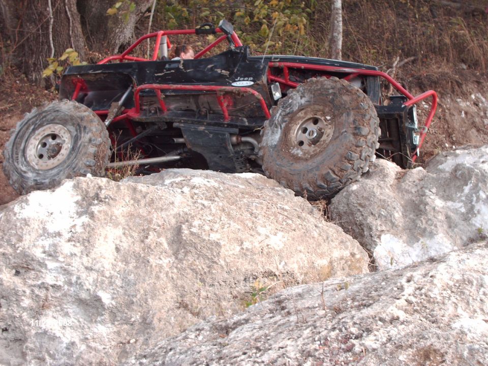 Modified Jeep with roll cage going over rocks. Looks like it's struggling