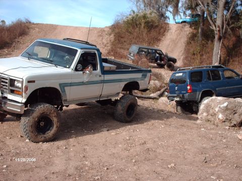 1982 Ford F-100 - Multiple off-road vehicles navigate a rocky, dirt trail on a sunny day.