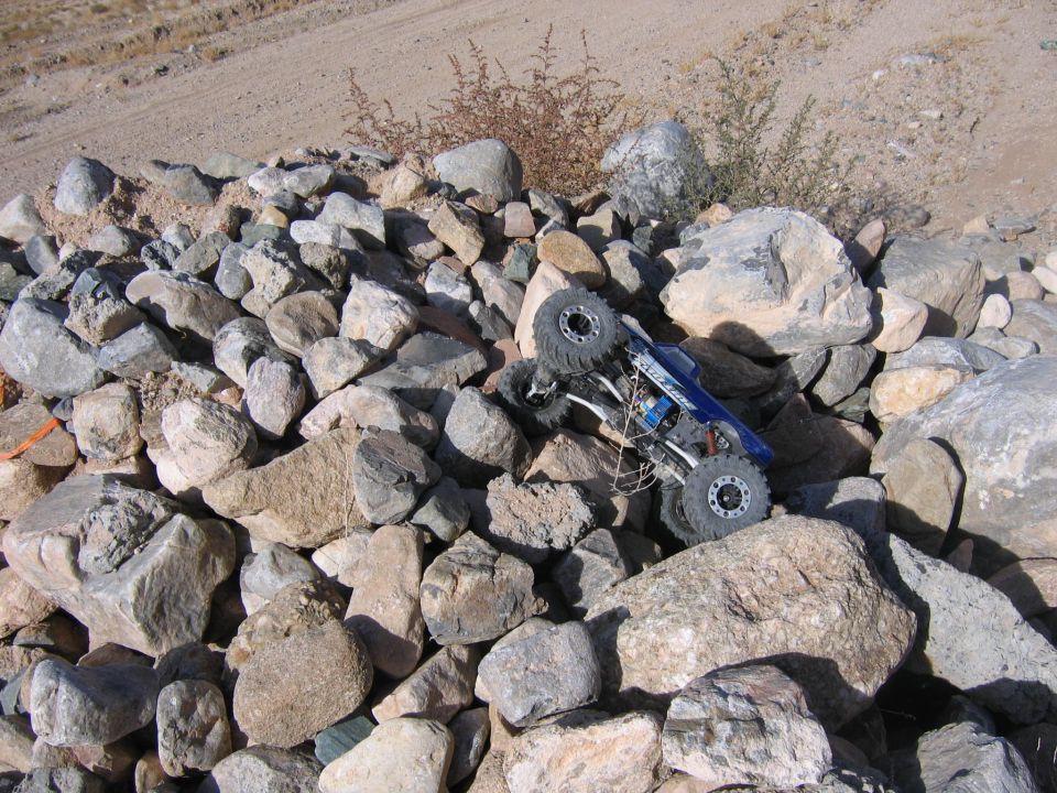 Blue remote control rock crawler on its side amidst a pile of large rocks