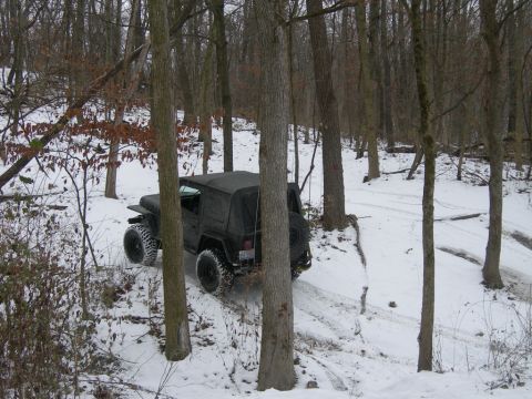 1991 Jeep Wrangler - A black Jeep Wrangler navigates a snowy path through a wooded area during winter.