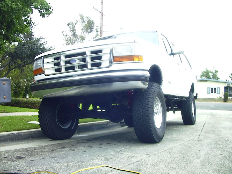 Lifted white Ford SUV on off-road tires, low front-quarter view on a suburban street