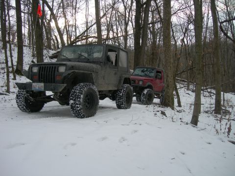 1991 Jeep Wrangler - Two off-road vehicles, a Jeep Wrangler and a Suzuki Samurai, navigate a snowy forest trail.