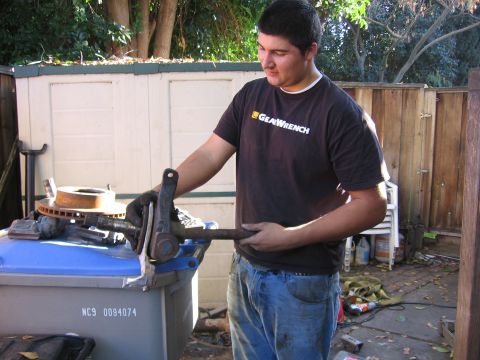 1989 Ford Bronco - A man holds a car suspension component, with a brake rotor visible on a blue trash bin in the foreground.