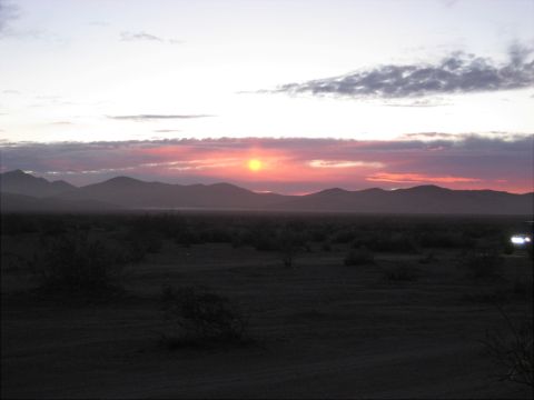 1996 Ford Bronco - A vehicle's headlights shine in the distance across a desert landscape as the sun sets behind mountains.