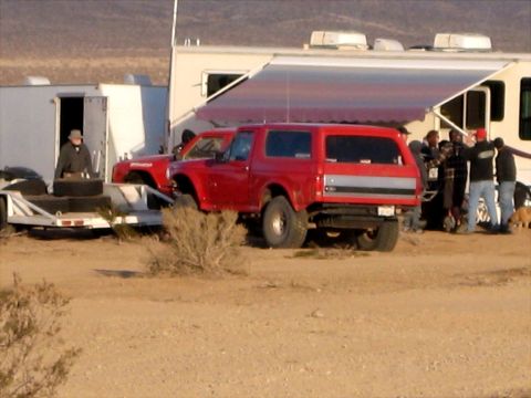 1996 Ford Bronco - A red SUV with a silver stripe and off-road tires is parked near an RV and another vehicle.