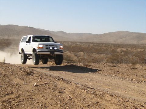 1996 Ford Bronco - White 1996 Ford Bronco jumps a dirt road in the desert.
