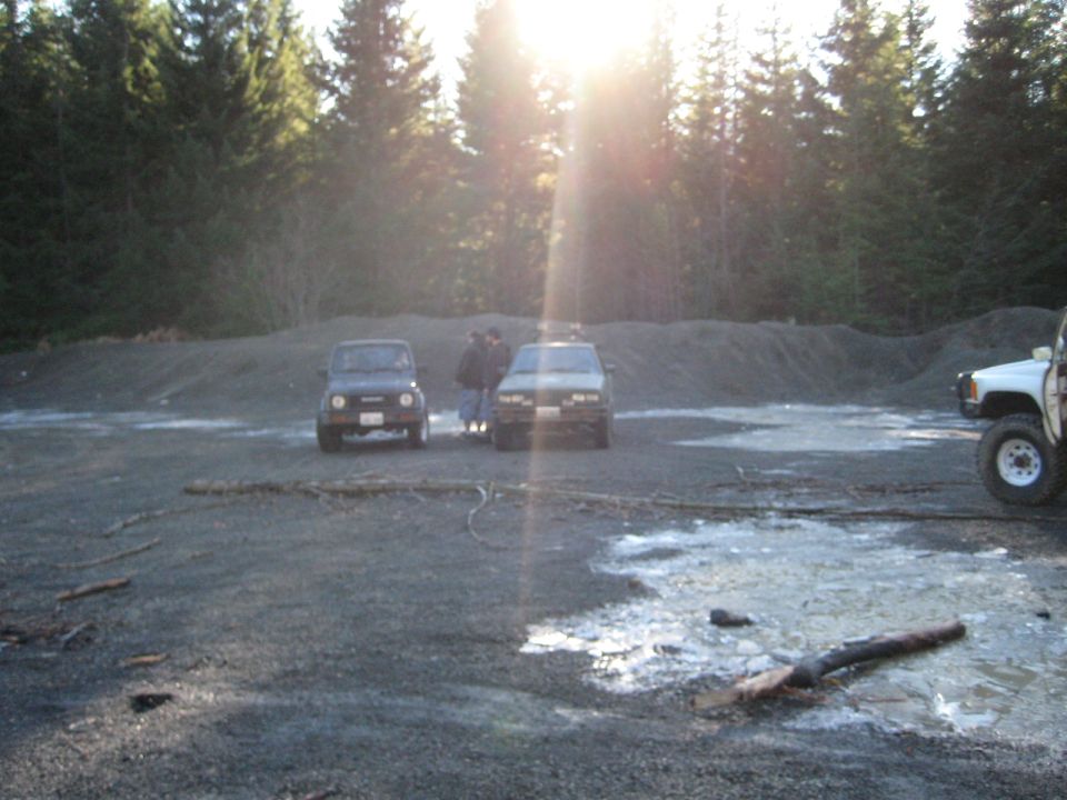 Three SUVs parked on gravel with trees in the background and sun glare