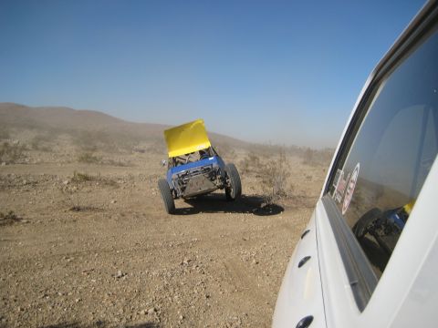 1996 Ford Bronco - An off-road buggy with its hood up is seen tilted on a dusty trail, with another vehicle in the foreground.
