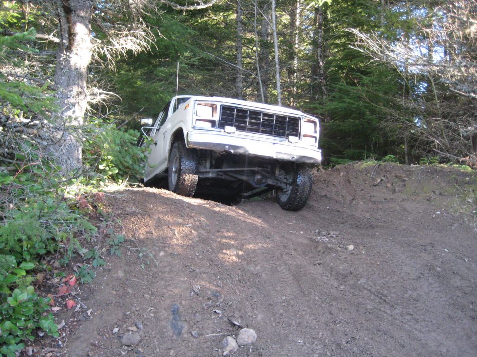 White 1980 Ford Bronco driving on a dirt hill with trees in the background