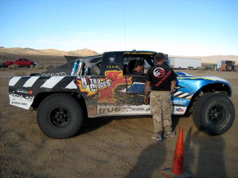 1996 Ford Bronco - Desert race truck with custom graphics and sponsor decals. A red pickup is parked in the background.