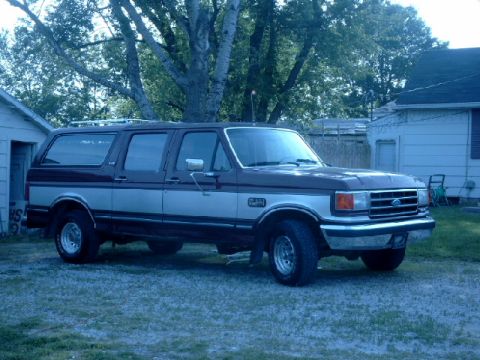 1990 Ford Bronco - This two-tone Ford Bronco SUV is parked in a grassy yard with houses in the background.