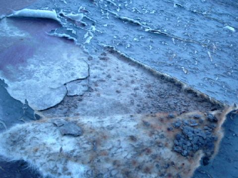 1990 Ford Bronco - The paint is flaking off, revealing rust and damage underneath on this vehicle panel.