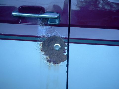 1990 Ford Bronco - A significant rust hole is visible on the side of a vehicle's door.