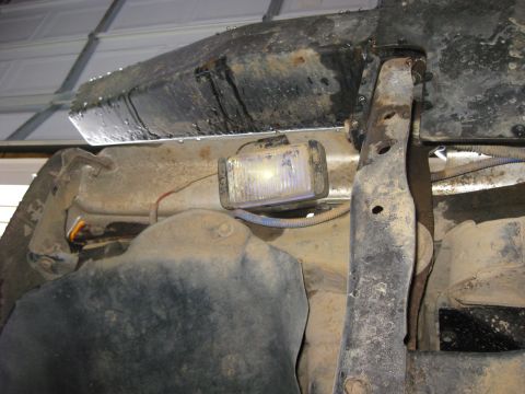 1979 Ford Bronco - Close-up of a rock light installed on the undercarriage of a vehicle, showing rusty frame components.