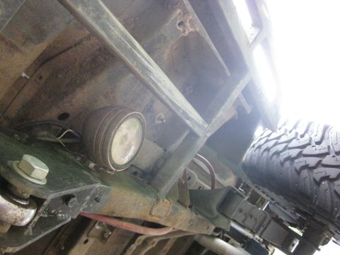 1979 Ford Bronco - Underside view of a vehicle, focusing on a rock light and tire. Frame and suspension parts are visible.