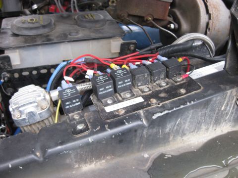 1979 Ford Bronco - Close-up view of the engine bay, focusing on the electrical relay system and an air compressor unit.