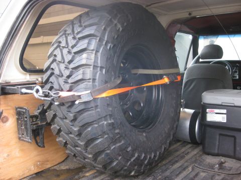 1979 Ford Bronco - Interior view of a vehicle's cargo area with a large spare tire mounted, alongside a storage container.