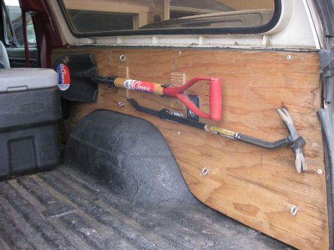 1979 Ford Bronco - Tools are organized and mounted on the interior wall of a vehicle, including a shovel and a crowbar.