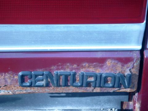 1990 Ford Bronco - The 'CENTURION' emblem is visible on a heavily rusted section of a vehicle's body panel.