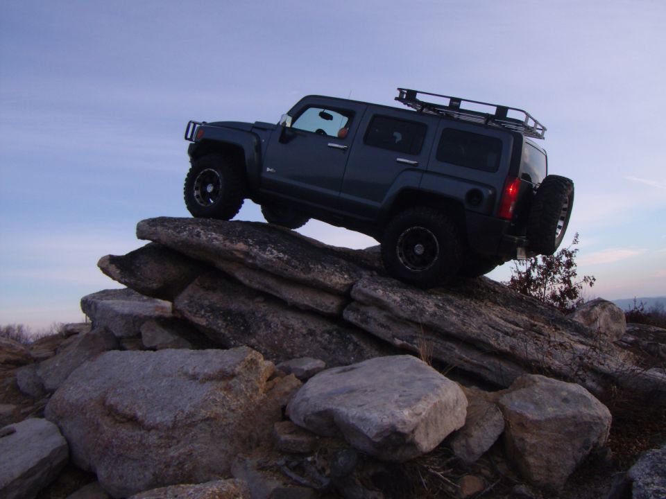 Dark gray Hummer H3 climbing over large rocks on an overcast day