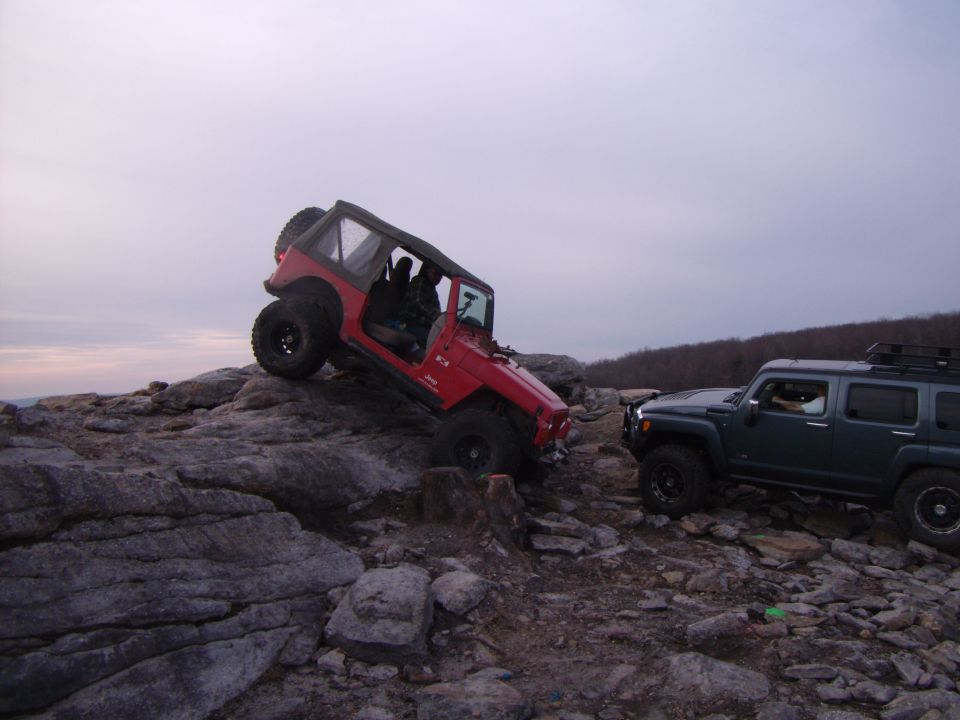 Red 2003 Jeep Wrangler climbing rocks, dark grey Hummer H3 parked nearby
