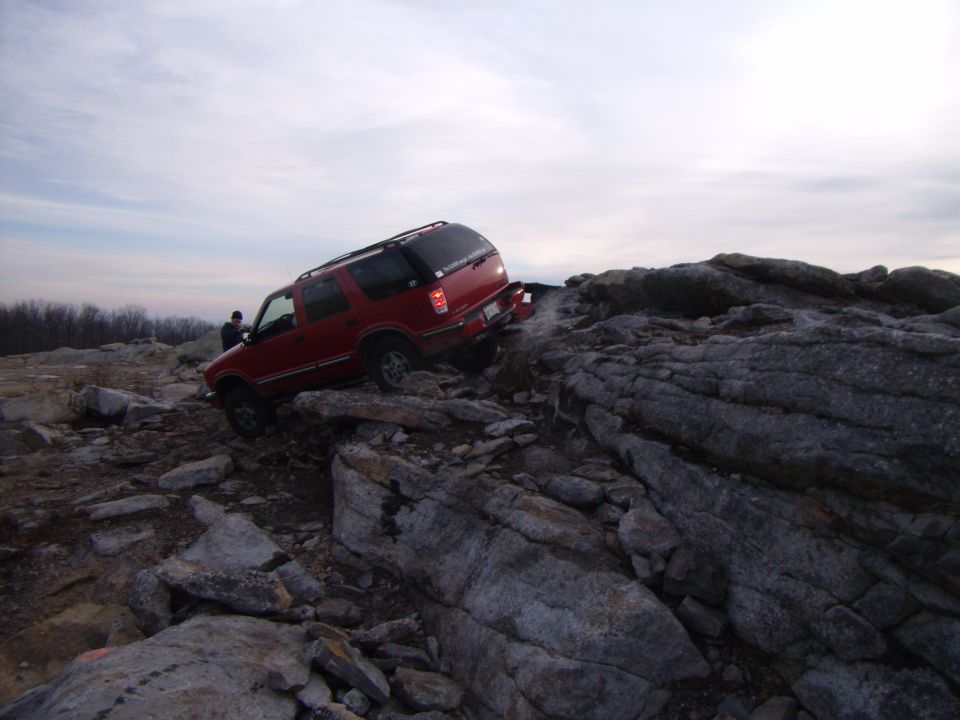 Red SUV climbing over large rocks on an off-road trail