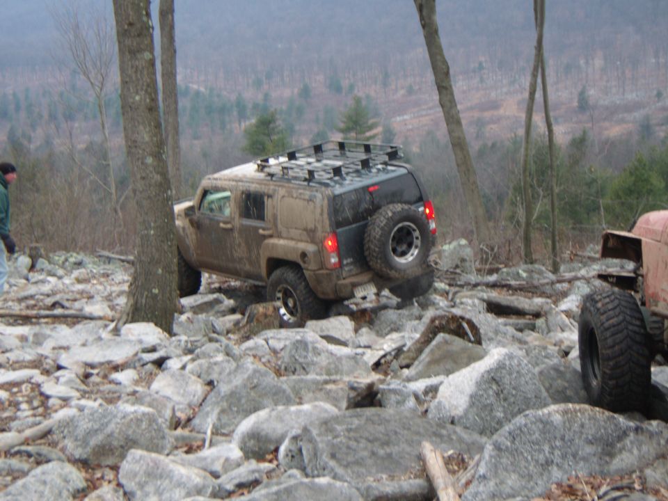 Muddy Hummer H3 navigating a rocky trail with another vehicle visible